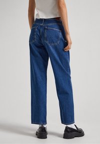 Jeans anchos de mezclilla de color azul, con dos bolsillos traseros y una cintura alta. Combinados con zapatos de plataforma negros y calcetines blancos.