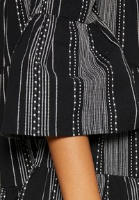 Tissu noir avec un motif à rayures verticales blanches et de petits détails en points. Le matériau a une texture douce et comprend des accents froncés.