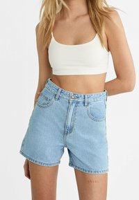 Pantalones cortos de mezclilla azul claro con cintura alta, cinco bolsillos y cremallera en la parte delantera. La tela tiene una textura suave y un desgaste mínimo.