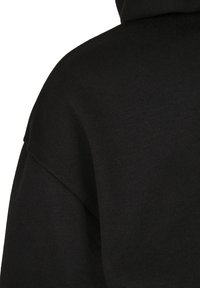 Svart huvtröja med ett mjukt, texturerat tyg och en avslappnad passform. Noterbara designelement inkluderar en vid halsringning och sänkta axlar.