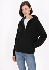 Mustat fleece-takki, jossa on vetoketju edessä, huppu ja sivutaskut; sileä pinta, rento muotoilu ja hieman ylipitkä malli.