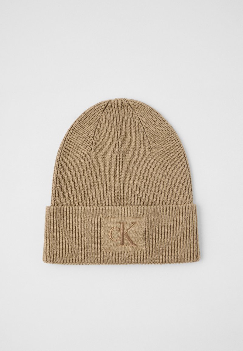 Brūns adīts cepure ar ribotu tekstūru un salocītu piedurkni. Priekšā ir neliels izšūts "CK" logs.