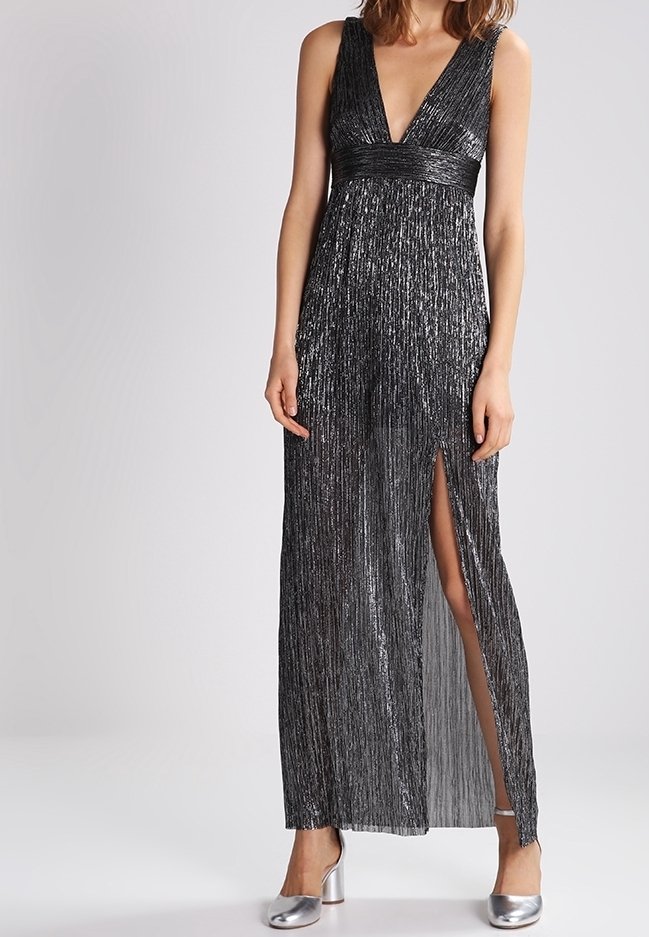 Maxi dress in black with metallic vertical stripes, deep V-neck, and waist accent. Features a thigh-high slit and a flowing silhouette. Silver heels.