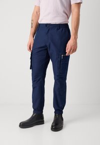 Marine cargo bukser med elastiske manchetter, som har flere lommer, inkludert en glidelåslomme med denimdetaljer. Strukturert stoff.
