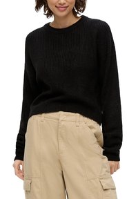 Schwarzer gerippter Strickpullover mit Rundhalsausschnitt, kombiniert mit khakifarbenen Cargo-Hosen, die seitliche Taschen und eine lockere Passform bieten.