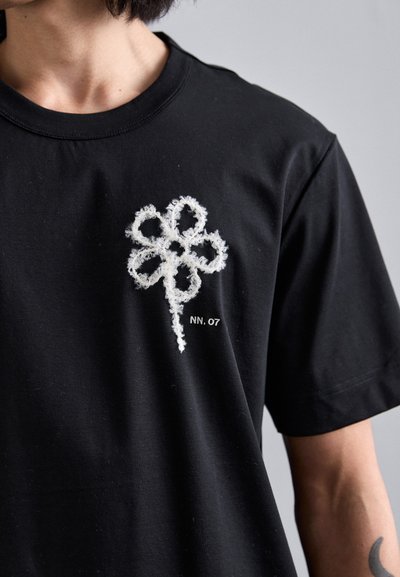 Sort bomulds T-shirt med et hvidt broderet firkløverdesign og teksten "NN. 07" under grafikken. Korte ærmer.