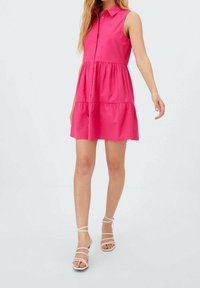 Vaaleanpunainen hihaton mekko, jossa on nappisuljenta edessä, röyhelömäinen kerroksellinen hame ja kaulus. Yhdistetty paljasvärisiin, remmillisiin sandaaleihin.