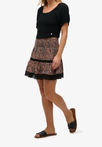 Top corto smockato nero con maniche puff corte, abbinato a una gonna in stampa paisley multicolore con bordo in pizzo e vita nera.
