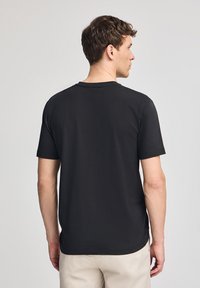 Camiseta negra de manga corta con escote redondo y aberturas laterales, hecha de una tela suave, que presenta una textura lisa y un ajuste casual.