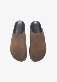 Rudos zomšiniai slip-on batai su lygiu juodu vidumi ir apvaliu pirštu, turintys minimalų siuvinėjimą ir tekstūruotą paviršių.