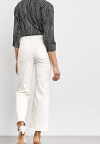 Jean blanc taille haute avec un motif texturé, ourlet effiloché, associé à une chemise rayée noire et blanche avec des manches retroussées.