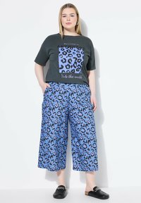 Czarna koszulka z akcentem w leopardzie i napisem. Niebieskie spodnie w szerokim kroju w leopardzie z czarnymi akcentami. Czarne buty wsuwane z detalem łańcucha.