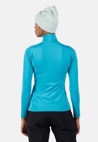 Lichtblauw lange mouwen sporttop gemaakt van rekbare stof, met een ritssluiting bij de hals en een aansluitende snit, gecombineerd met een mintgroene gebreide beanie.
