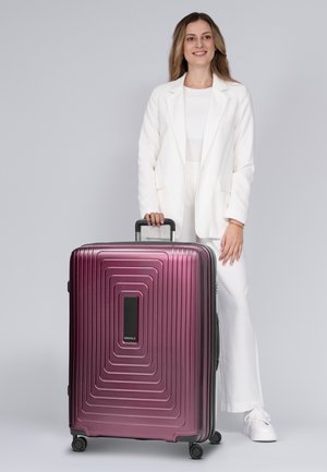 Hard-shell koffers in een glanzende bordeauxrode kleur met een gestructureerd golfpatroon, uitschuifbare handgreep en vier wielen voor mobiliteit.