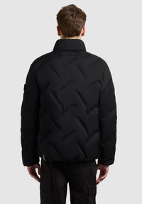 Veste matelassée noire avec un motif en losanges, col montant et poignets côtelés. Présente une étiquette logo près de l'encolure.