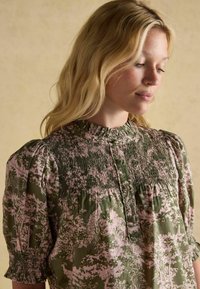 Roheline ja roosa mustriga pluus, millel on smockimisega bodice, gathered lühikesed varrukad ja kõrge kaelus. Ees on nööbid.