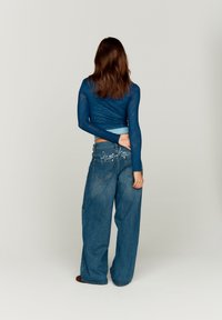 Blue long-sleeve top with textured fabric, paired with loose-fit blue denim jeans featuring back pockets and decorative stitching.