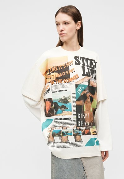 Γυναίκα που φοράει υπερμεγέθη λευκό μακρυμάνικο πουκάμισο με πολύχρωμο καλοκαιρινό θέμα και φωτογραφίες παραλίας, συνδυασμένο με ανοιχτόχρωμη τζιν φούστα.