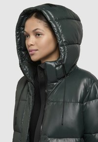 Donsjack in donkergroen, met een glanzende textuur, oversized capuchon, ritssluiting en verstelbare koorden bij de hals.