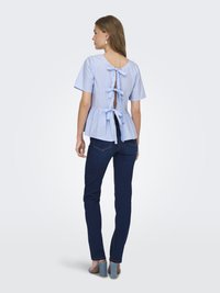 Haut peplum rayé bleu clair avec des manches courtes et un détail à nouer à l'arrière, associé à un jean en denim foncé et des sandales à talons bleu clair.