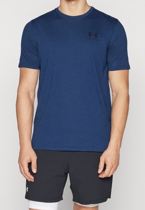 Homme portant un t-shirt bleu uni à manches courtes Under Armour et un short de sport noir Under Armour avec un short de compression blanc en dessous.