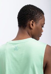 T-shirt sans manches vert menthe, en tissu coton, à encolure ronde, présentant un graphique de ciseaux bleu clair imprimé au dos.