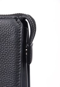 Sort lædertaske med en struktureret overflade, der har en lynlåslukning og en metalknap. Siden viser glatte og mønstrede områder.