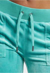Turkusowe dresy z miękkiej tkaniny, z ribbowym paskiem w talii, sznurkami z metalowymi akcentami i bocznymi kieszeniami.