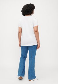 Hvit bomull t-skjorte med kort erm og rund hals, kombinert med blå flare jeans. Enkelt, udetaljert design.