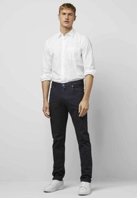 Chemise blanche à boutons, jean bleu marine avec une ceinture noire, baskets blanches ; coupe ajustée, tissu lisse et détails minimalistes.