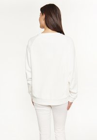 Felpa bianca con una vestibilità rilassata, maniche raglan e polsini a coste. Tessuto di cotone liscio, design minimalista e senza motivi o loghi visibili.
