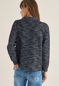 Maglione blu navy con texture e maniche lunghe, caratterizzato da un motivo sottile. Design casual abbinato a jeans azzurri chiari, che mostrano una vestibilità rilassata.