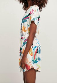 Bloemenprint jurk van lichte stof, met een witte basis en kleurrijke ontwerpen, korte mouwen en een ceintuur in de taille voor een gedefinieerde vorm.