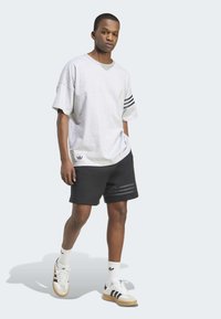 Šedé oversized tričko s černými pruhy, spárované s černými šortkami s horizontálním pruhovaným vzorem. Doplneno bílými teniskami a ponožkami.