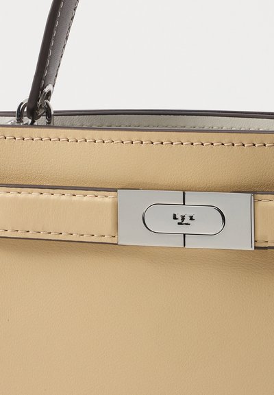 Beige læderhåndtaske med en glat overflade, prydet med en sølvklap og kontrasterende mørke syninger. Enkel og struktureret design.