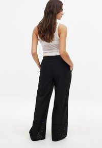 Čierne široké nohavice s uvoľneným strihom, s vystrihnutými detailmi na spodnom okraji a elastickým pásom pre pohodlie.