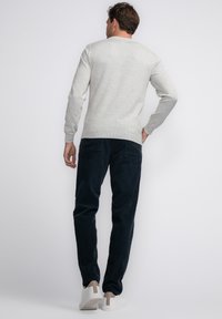 Lichtgrijze gebreide trui met geribde manchetten, gecombineerd met donkerblauwe corduroybroek met achterzakken en een gladde textuur. Witte schoenen maken de look compleet.