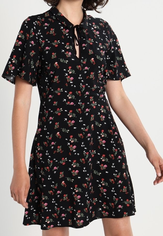 Robe noire à manches courtes avec un petit imprimé floral rose et rouge et un décolleté en goutte noué avec un nœud.