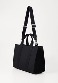 Sort stofhåndtaske med to tophanke og en aftagelig, justerbar skulderrem. Har en struktureret form og tekstureret overflade.