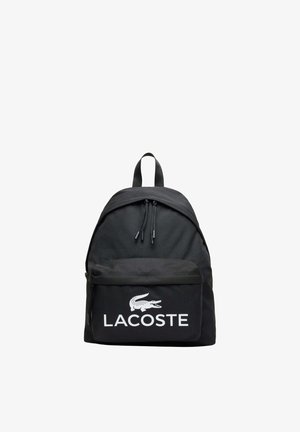 Mochila negra con bolsillo frontal con cremallera que presenta el logo blanco de Lacoste y el nombre de la marca, doble tirador de cremallera y asa superior para llevar.