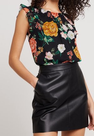 Femme portant un haut sans manches noir à fleurs avec des volants et une jupe en cuir noire taille haute avec poches.