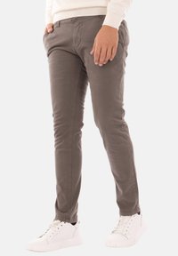 Chino slim-fit verdi oliva in tessuto di cotone, con tasche laterali e passanti per cintura, abbinati a sneakers bianche per un look casual.