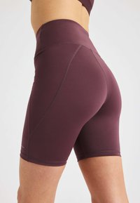 Shorts da allenamento bordeaux con vita alta, texture liscia e cuciture piatte. Lunghezza a metà coscia senza motivi o dettagli visibili.