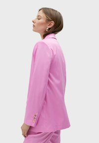 Pink blazer with a tailored fit, features a notched collar, long sleeves, and gold button accents on the cuffs. Smooth, lightweight material.
