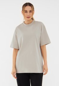 Világosszürke, oversize póló rövid ujjakkal és kerek nyakkivágással, puha pamut anyagból készült, laza illeszkedéssel.