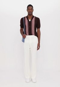 Brown short-sleeve shirt with pink vertical stripes, white drawstring pants, and white sneakers, complemented by a blue crossbody bag.
