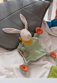Soft plush rabbit toy with a beige face, green body, orange-striped ears, and a yellow scarf, lying on a gray and white textured blanket.