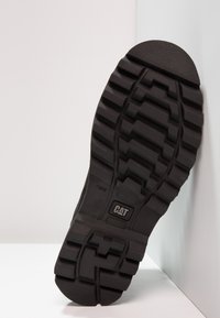 Suela de zapato de goma negra con patrón de relieve profundo, que presenta un logo de CAT y acentos texturizados para agarre y durabilidad.