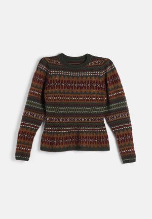 Femme portant un pull à motifs, une chemise blanche à col volanté, un pantalon en velours vert foncé, des bottines marron et un sac à épaule noir.