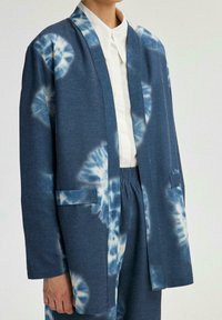 Chaqueta de kimono de color azul con un patrón, detalles de tie-dye en azul claro, mangas largas y dos bolsillos frontales, hecha de una tela suave y texturizada.